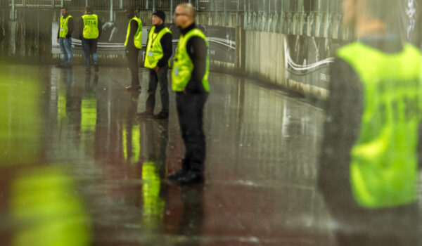 Security employees standing in a line at a stadium on a sporting event at night.